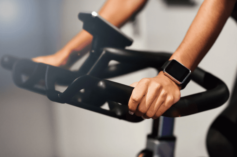 Nahaufnahme von H&auml;nden, die einen Spinner-Bike-Lenker halten, mit einer Sportuhr am Handgelenk.