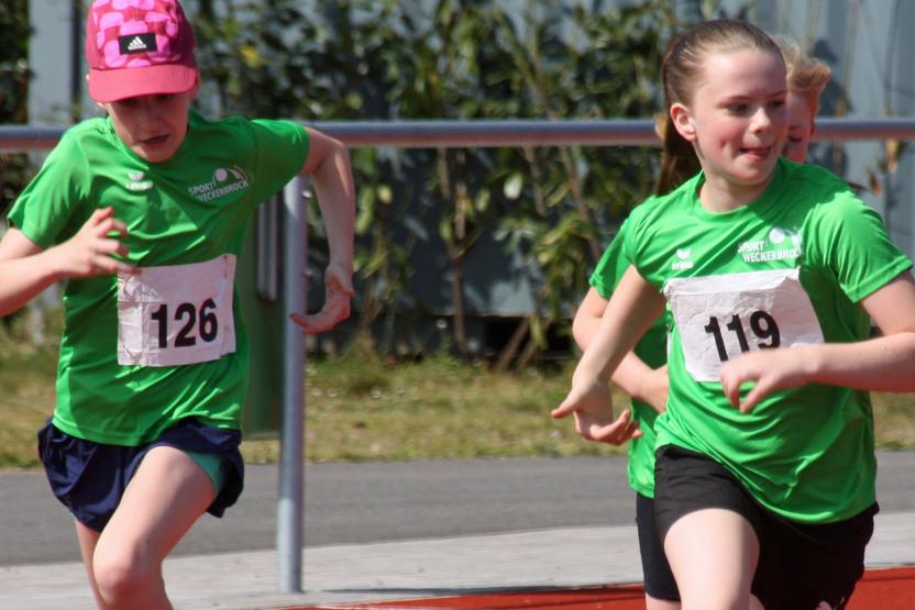 Zwei Kinder in gr&uuml;nen Trikots sprinten auf einer roten Laufbahn w&auml;hrend eines Wettkampfes.