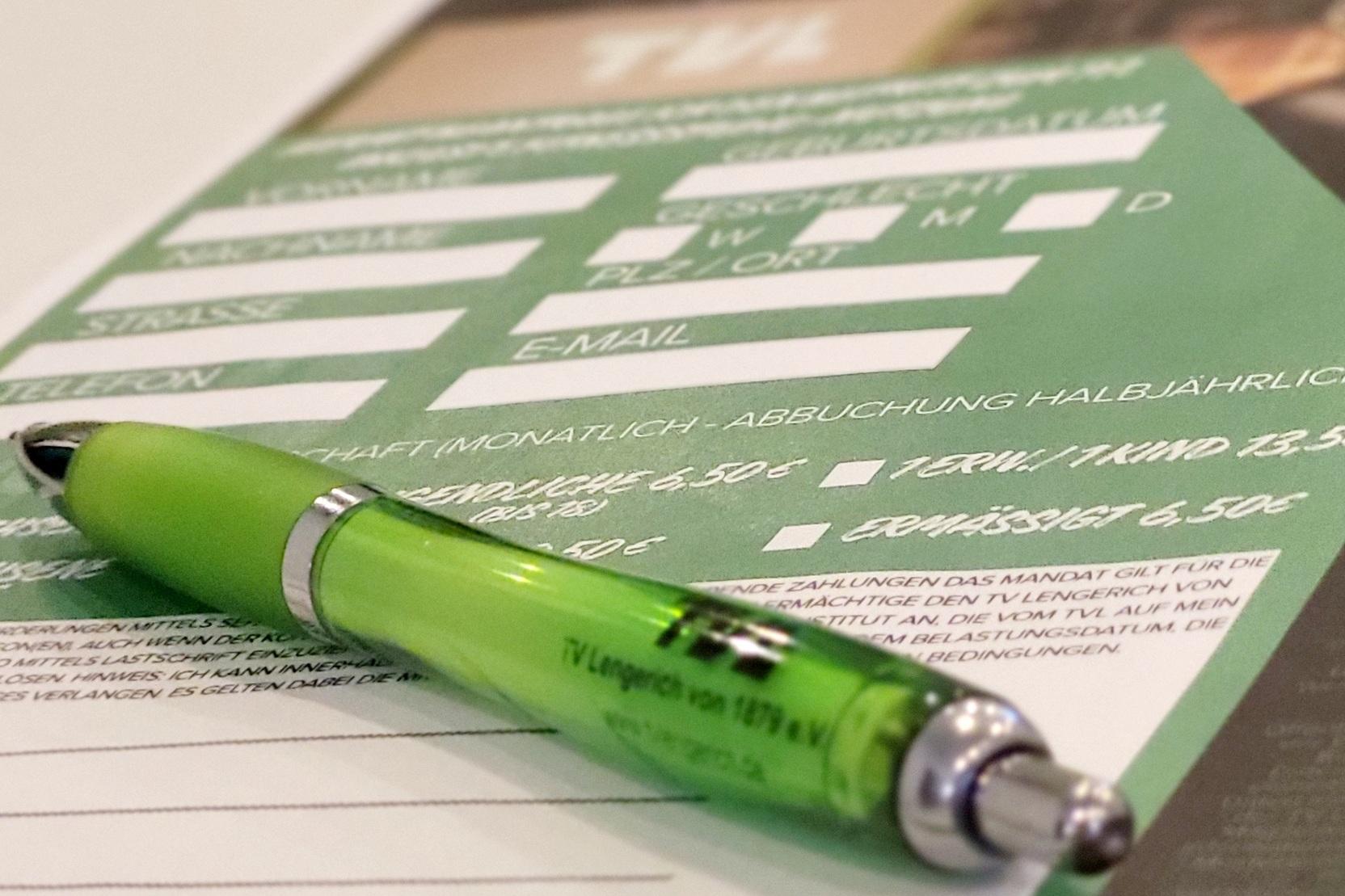 Gr&uuml;ner Stift liegt auf einem Formular mit Ausf&uuml;llfeldern in Wei&szlig; auf gr&uuml;ner Unterlage.