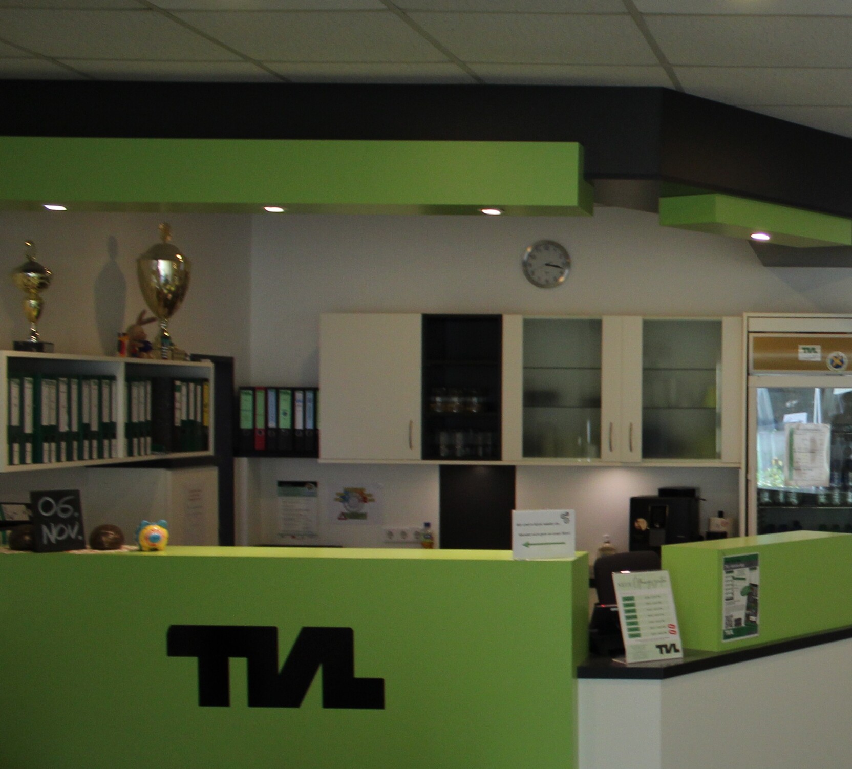 Lichtdurchfluteter Empfangsbereich mit gr&uuml;ner Theke, B&uuml;roschrank und digitalem Display an der Wand.