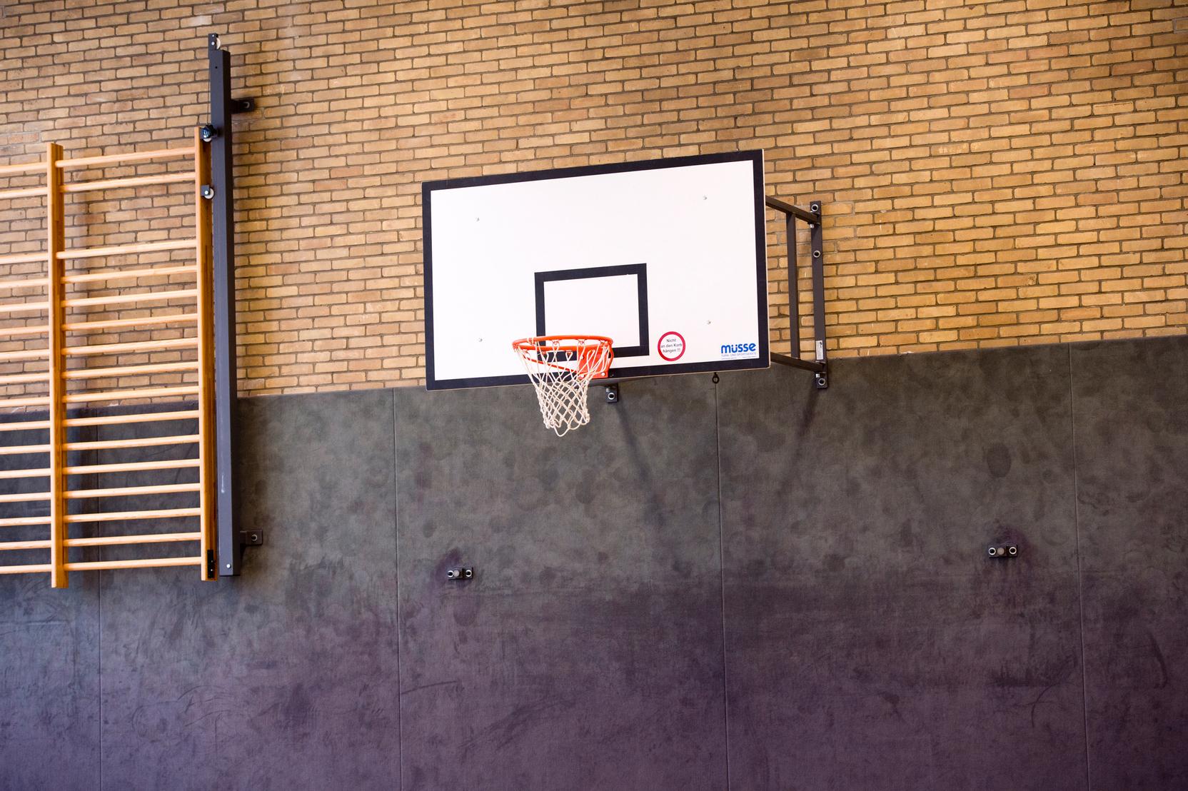 Basketballkorb an einer Wand mit Sprossenwand im Hintergrund in einer Sporthalle.