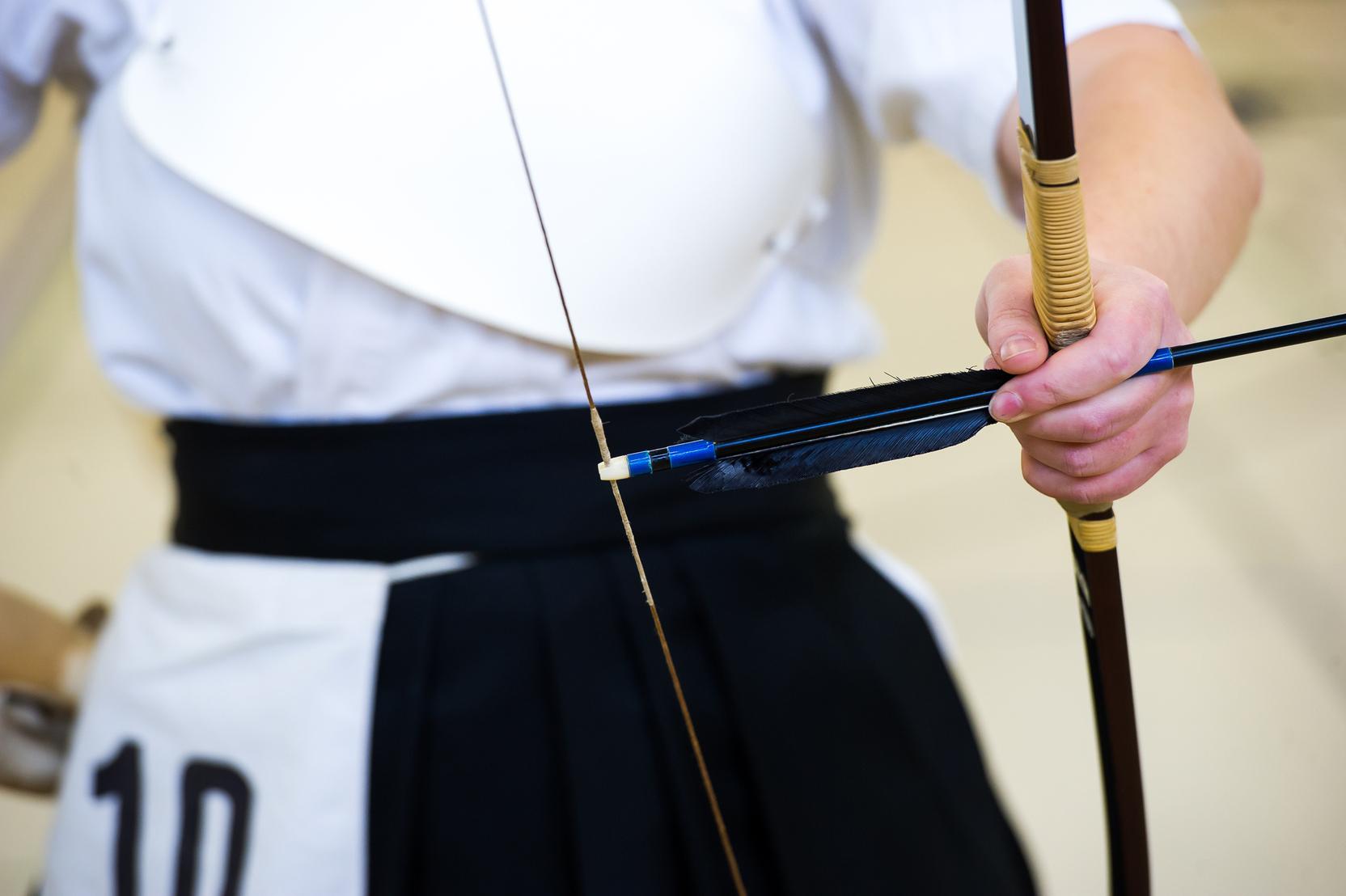 Nahaufnahme eines Bogenschützen, der einen Pfeil mit Feder auf eine gespannten Sehne anlegt.
