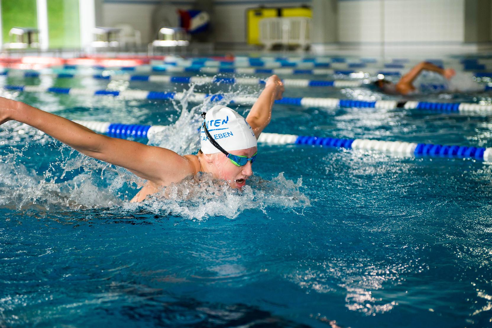 Junge Schwimmerin im Wettkampf, die im Wasser den Schmetterlingsstil ausführt, mit spritzenden Wassertropfen.